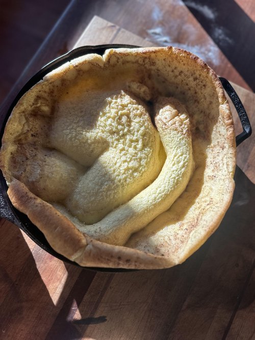 Dutch baby pancake baked in a cast iron skillet, showcasing a golden-brown, fluffy texture with a slightly crisp edge, placed on a wooden surface.