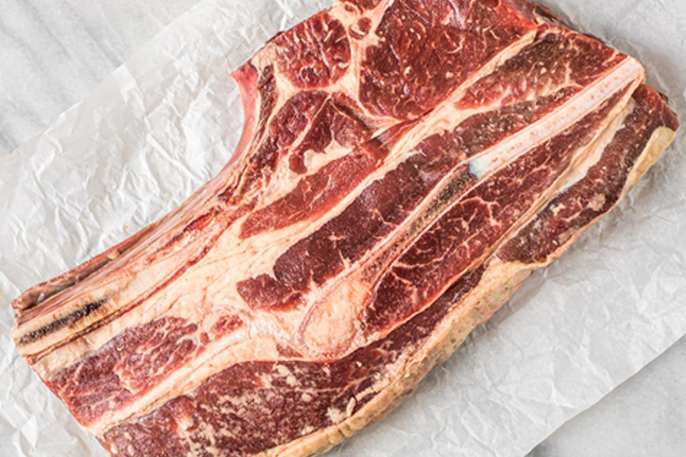 sequatchie.cove.farm.tennessee.grass.fed.beef.chuck.roast Raw ribeye steak displayed on parchment paper, showcasing marbling and rich red color, ideal for grilling or roasting.